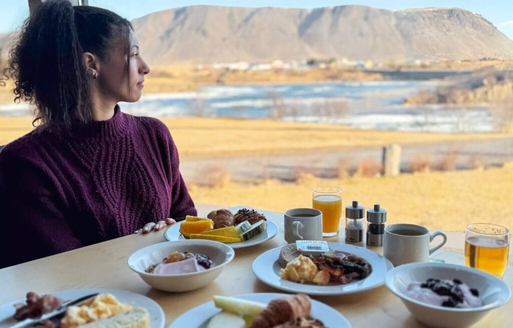 Woman in purple sweater enjoying breakfast with Icelandic landscape in background.