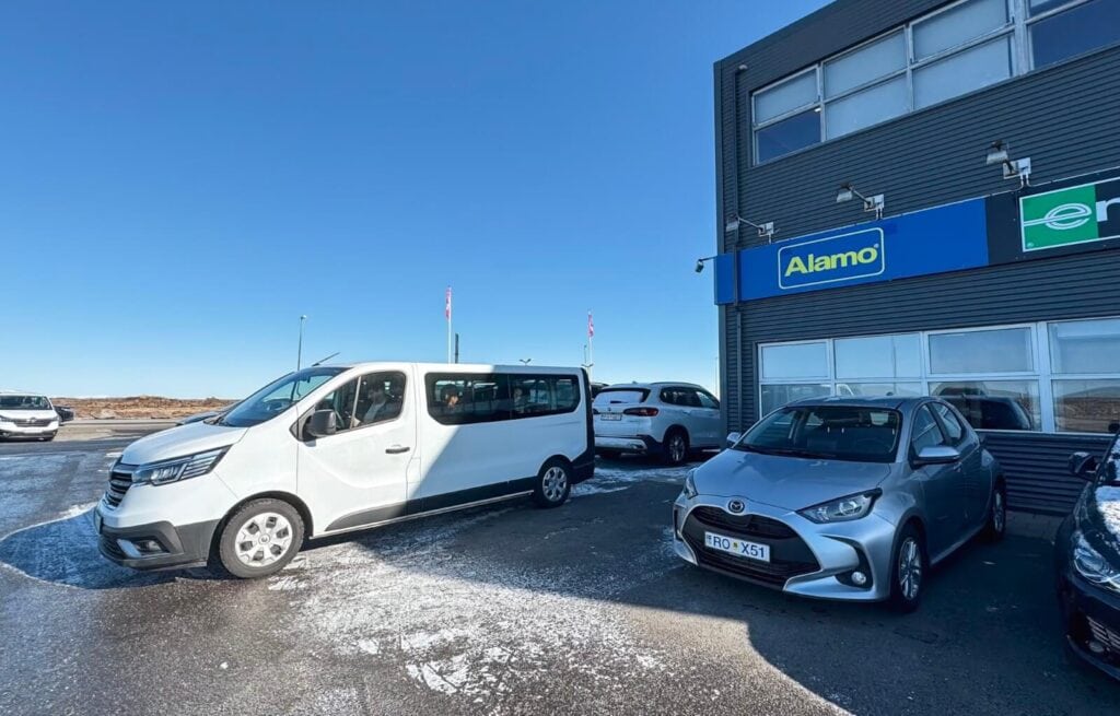 White van and grey car parked outside a building with Alamo sign in Iceland.