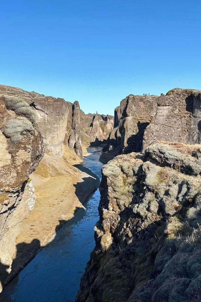 View of Fjaðrárgljúfur canyon with steep rocky cliffs and a winding river under a clear blue sky.
