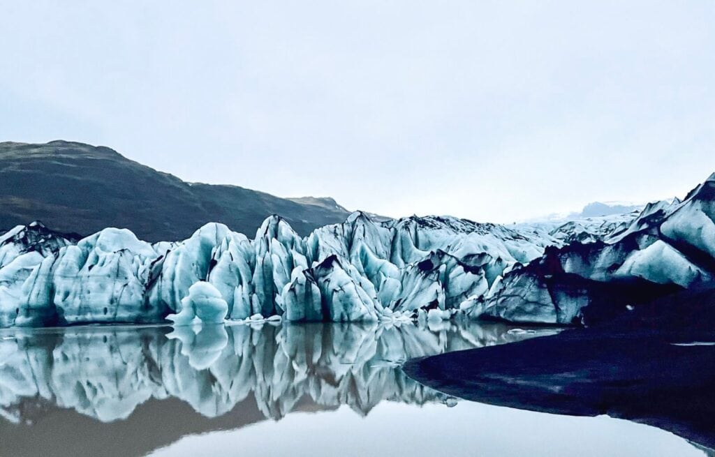 Glacier with jagged ice formations reflecting in calm water near Sólheimajökull, Iceland.