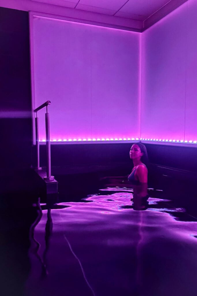 Woman relaxing in a purple-lit indoor pool with modern decor and ambient lighting.