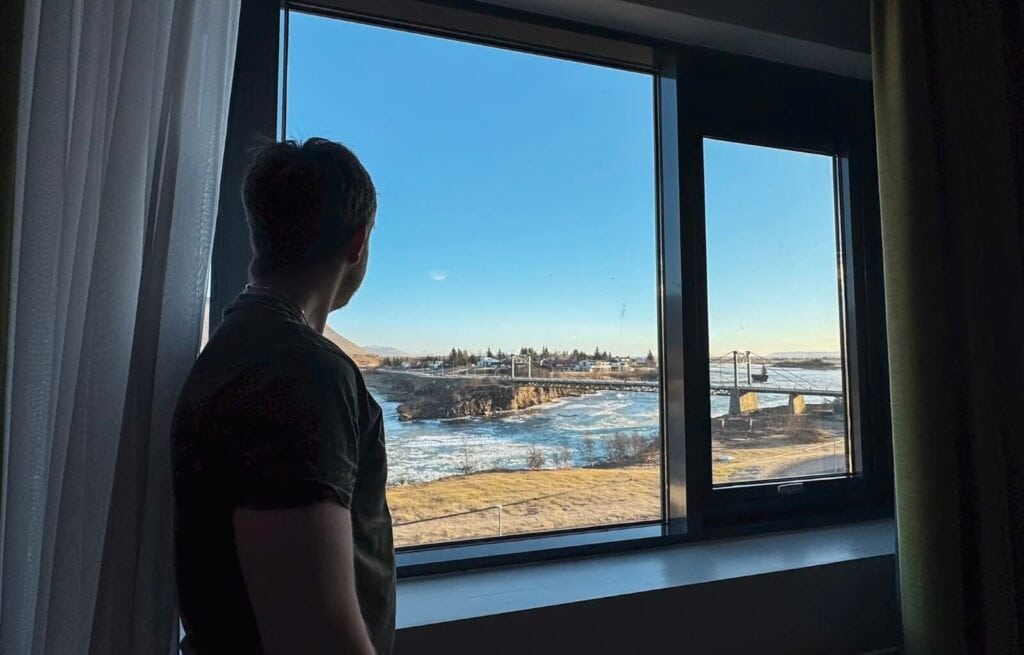 Person looking out of a window at snowy landscape and blue sky in Iceland.