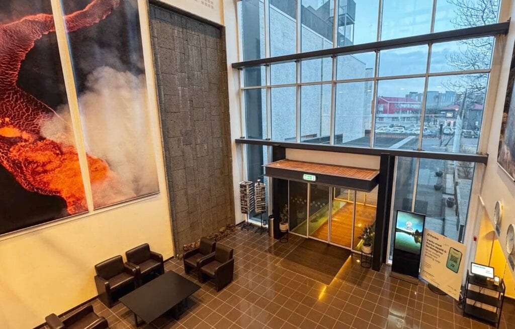 Modern hotel lobby with large glass windows, seating area, and volcanic eruption artwork on the wall.