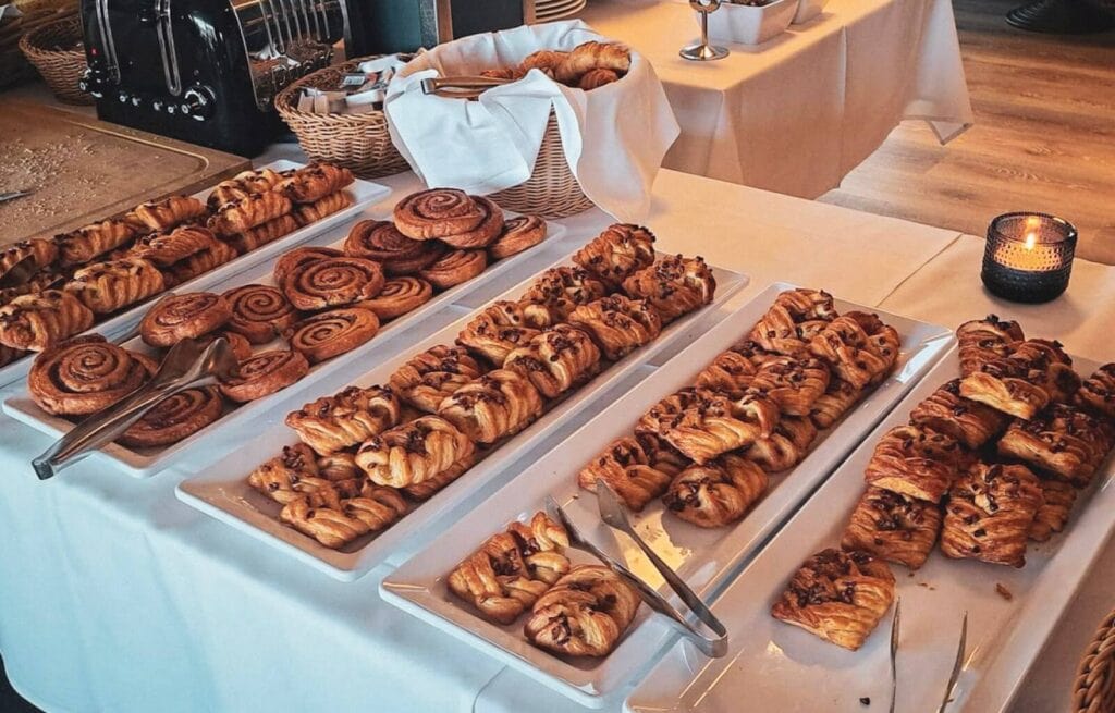 Assorted freshly baked pastries including cinnamon rolls, croissants, and Danish pastries on a buffet table.