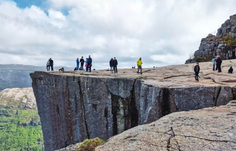 Tourists standing on a cliff edge overlooking a deep canyon in Stavanger, Norway.
