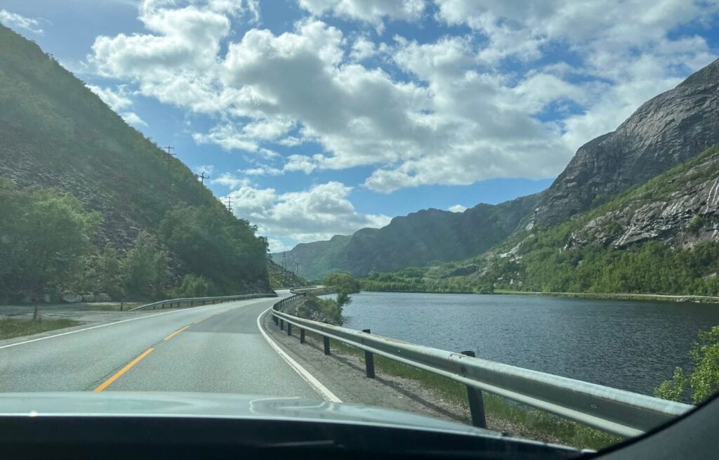 Scenic view of a winding road alongside a fjord with mountains and partly cloudy sky in Norway.