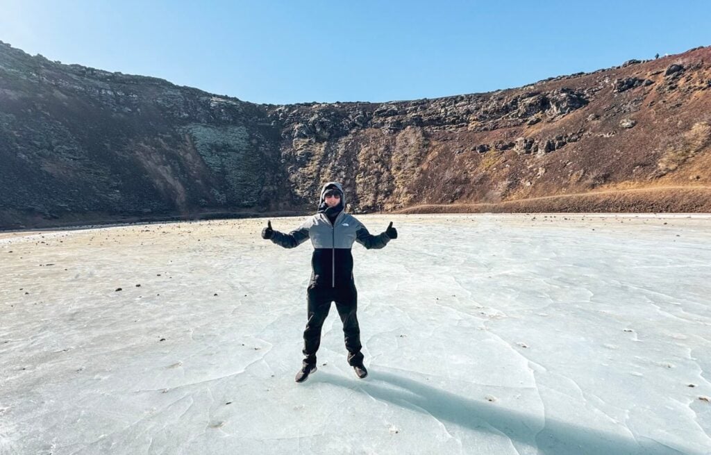 Person standing on icy landscape with mountains in the background under clear blue sky.