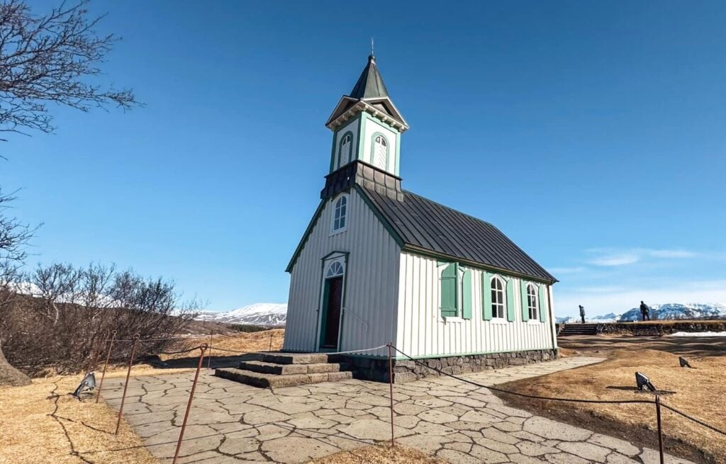 The beautiful church in Thingvellir National Park. It's white, green, and black, and the sky behind it is bright blue.