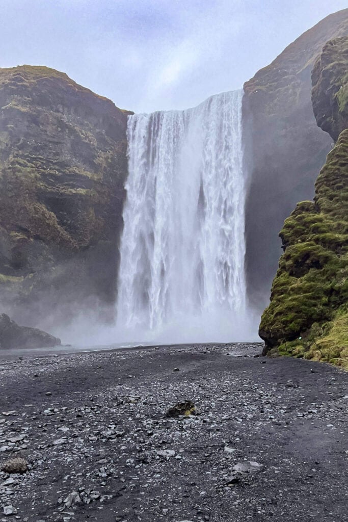Majestic waterfall cascading down moss-covered cliffs in Iceland with mist rising at the base.