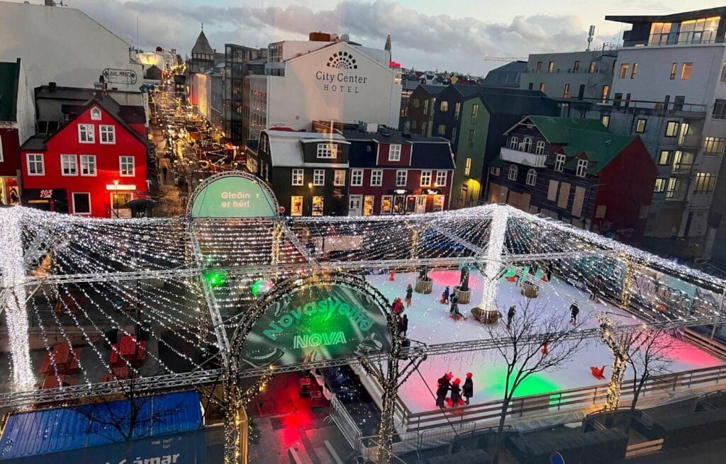 Ice skating rink in a city square decorated with festive lights and illuminated structures during winter.