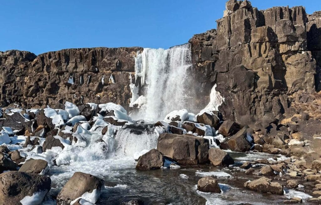 Oxarafoss waterfall hike in Thingvellir National Park - With a blue sky behind it. The waterfall tumbles dramatically off the rocks