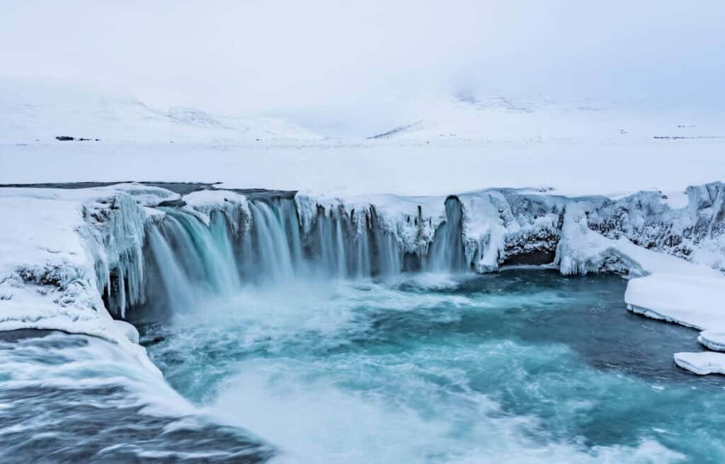 Frozen Godafoss waterfall with icy edges and flowing water in a snowy landscape in Iceland.
