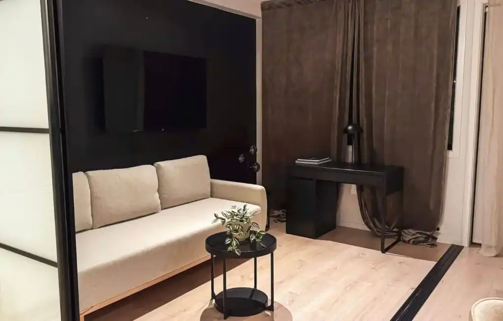 Modern living room with beige sofa, black TV, small round coffee table, and a black desk with a chair.