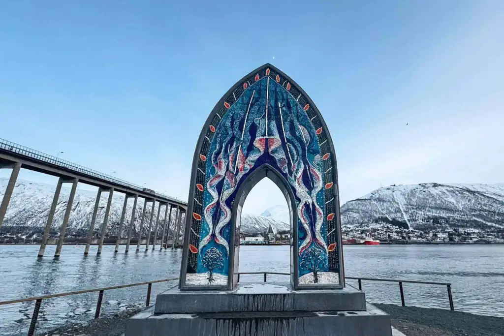 Colourful arched monument with intricate patterns, set against a fjord and snow-capped mountains in Tromso, Norway.