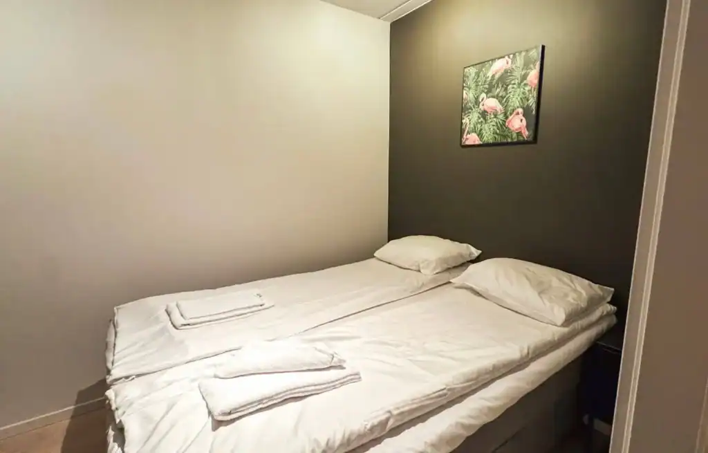 Simple hotel room with a double bed, white bedding, and a small picture of flamingos on the wall.