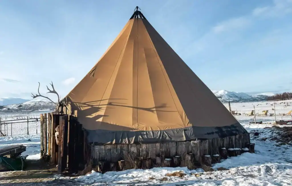 Traditional Sami tent with wooden base in snowy landscape under blue sky.