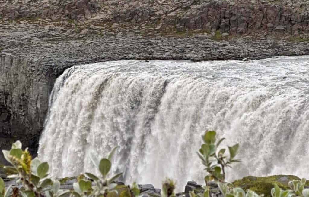 Majestic waterfall cascading over dark rocks with green foliage in the foreground.
