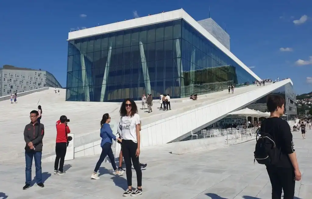 Modern glass building with people walking and standing outside on a sunny day.
