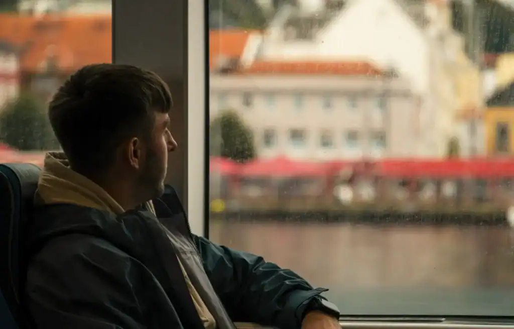 Man looking out of a train window at colourful buildings and water in Bergen, Norway.
