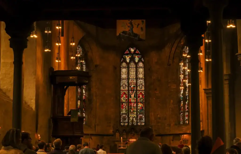 Inside a historic church with stained glass windows and wooden pews, filled with a congregation during a service.