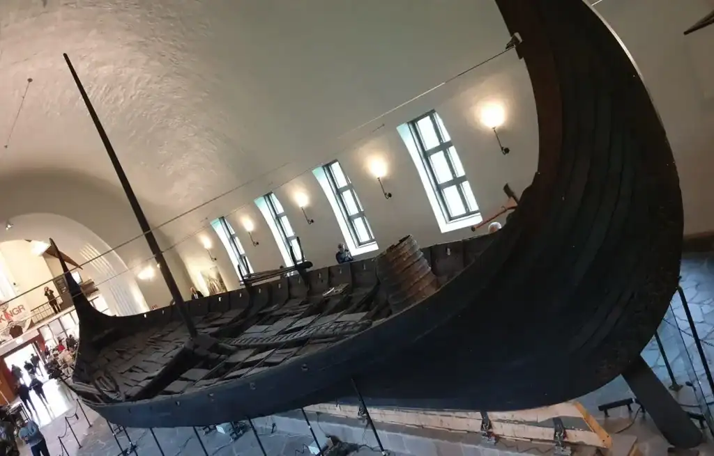Historic Viking ship replica displayed indoors with wooden structure and curved hull.