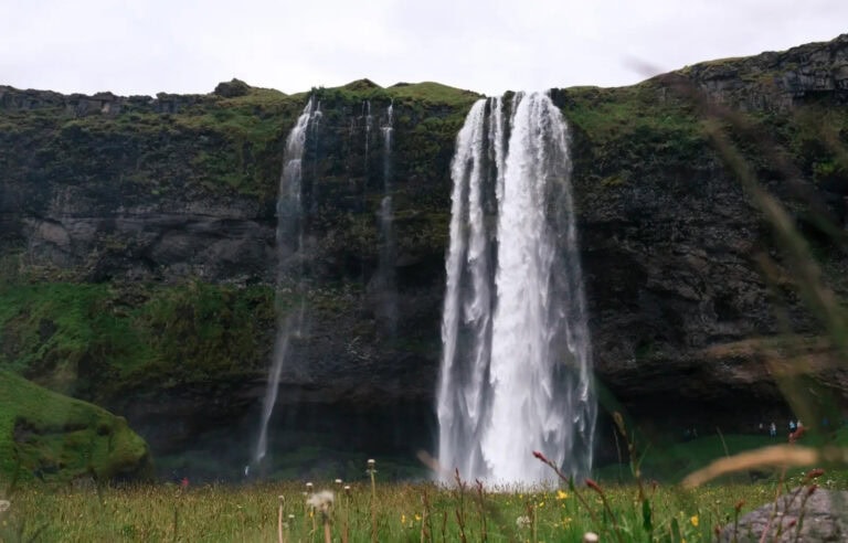 Majestic waterfall cascading down a cliff into a lush green field in Iceland.