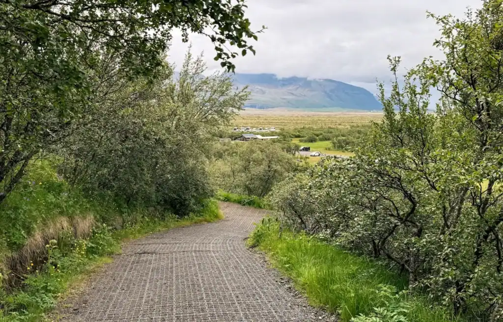 Gravel trail winding through lush greenery with distant mountains under cloudy sky.