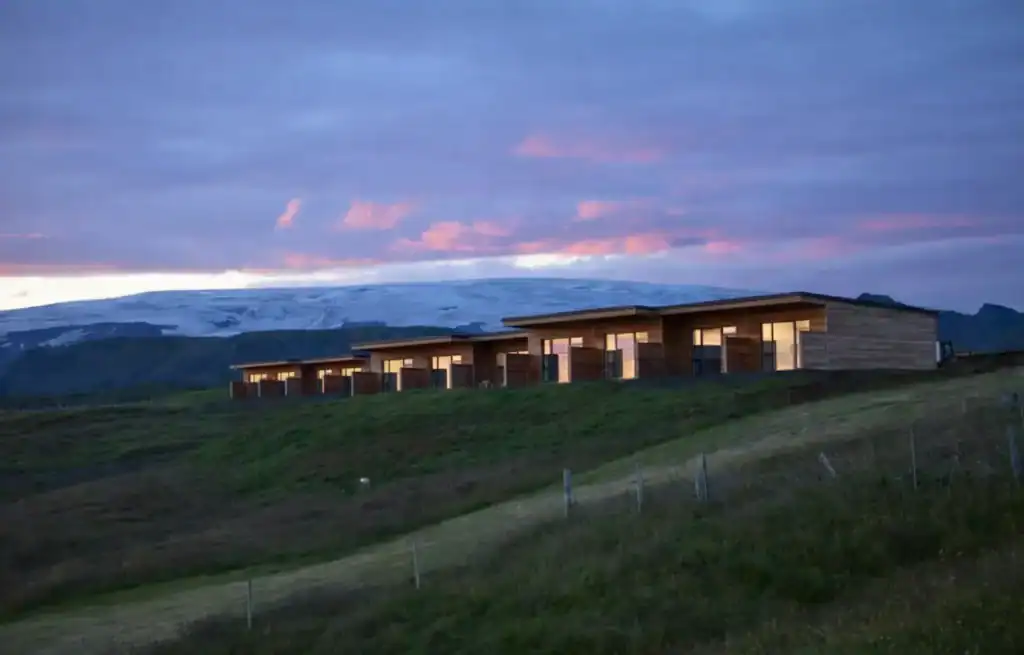 Modern wooden hotel building on a grassy hillside at dusk with a colourful sky.