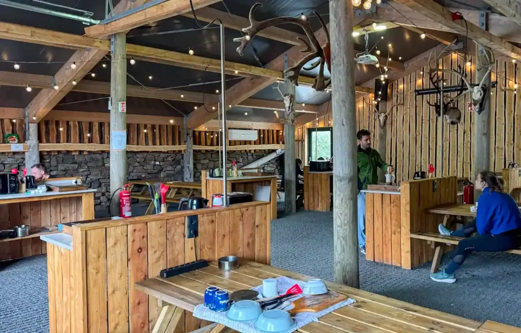 Interior of a rustic restaurant with wooden beams, hanging lights, and mounted animal trophies on the walls.