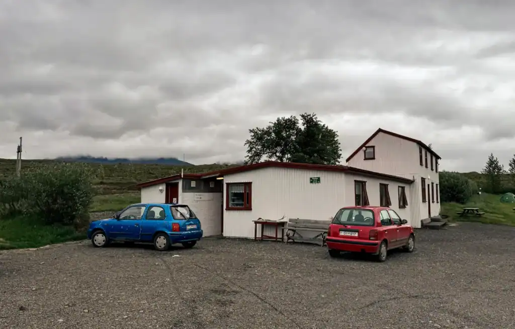 Two cars parked outside a white building under a cloudy sky in a rural setting.