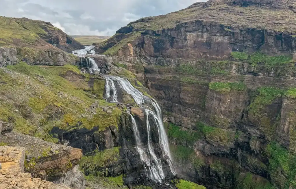 View of Glymur Waterfall cascading down a steep cliff in Iceland with lush green surroundings.