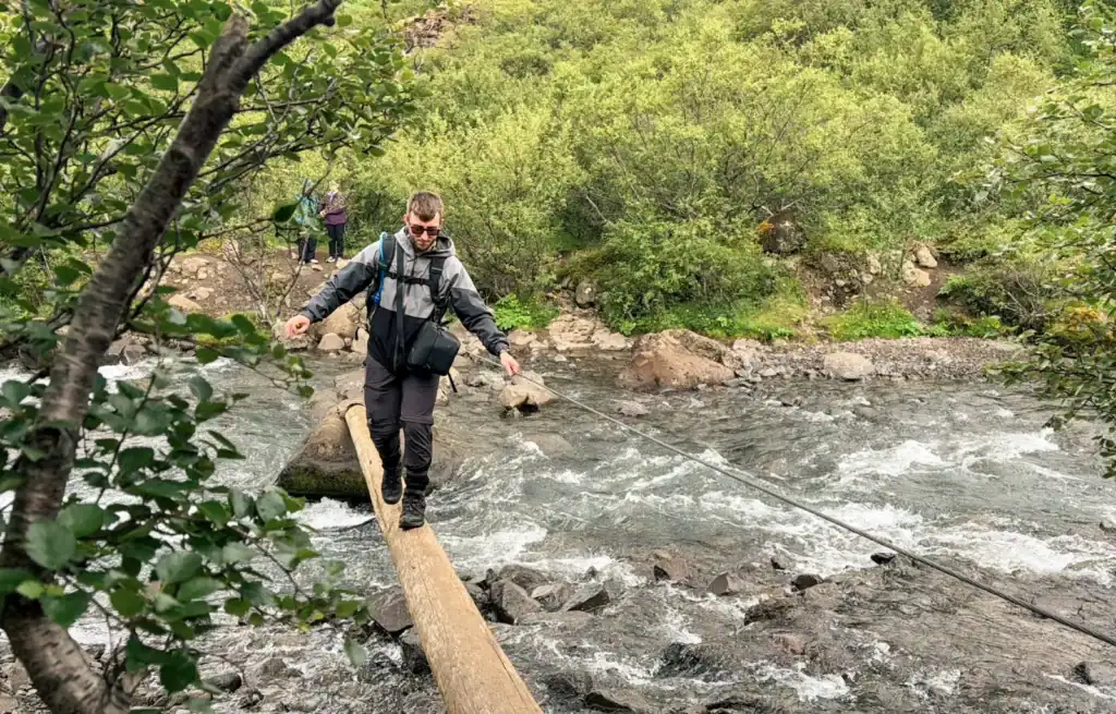 Hiker balancing on a narrow log bridge over a river in a lush green forest.