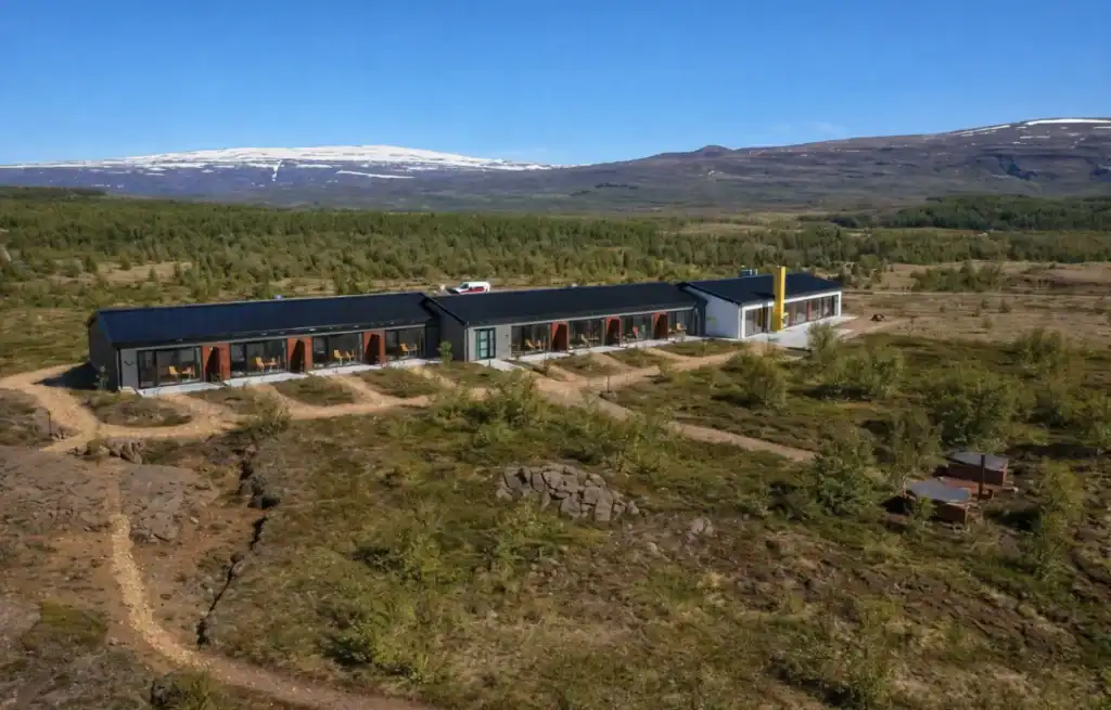 Modern single-storey building with black and grey exterior in Icelandic landscape with mountains and snow in the background.