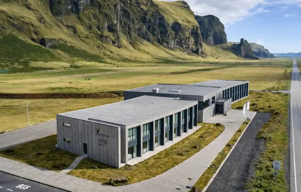 Modern building with large windows in a remote Icelandic landscape with mountains and open fields.