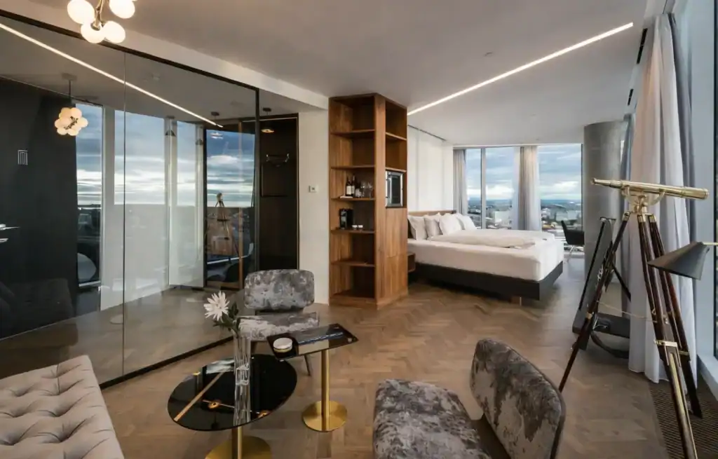 Modern hotel room with large windows, a telescope, and stylish furniture.